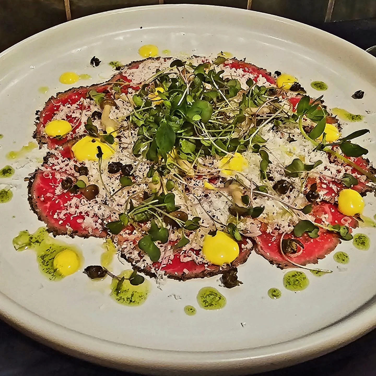 A colourful plate with greens, shaved cheese and small dots of sauce